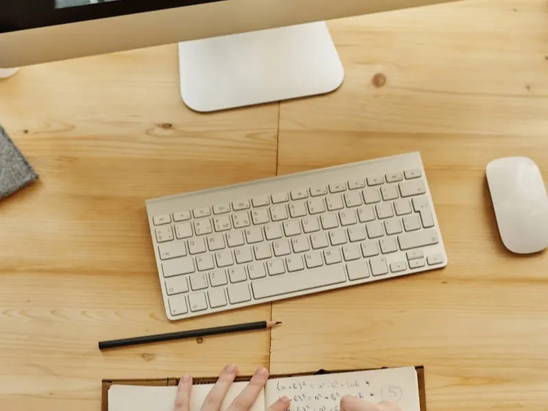 Student taking notes while participating in an online tutoring session with tutor visible on laptop screen