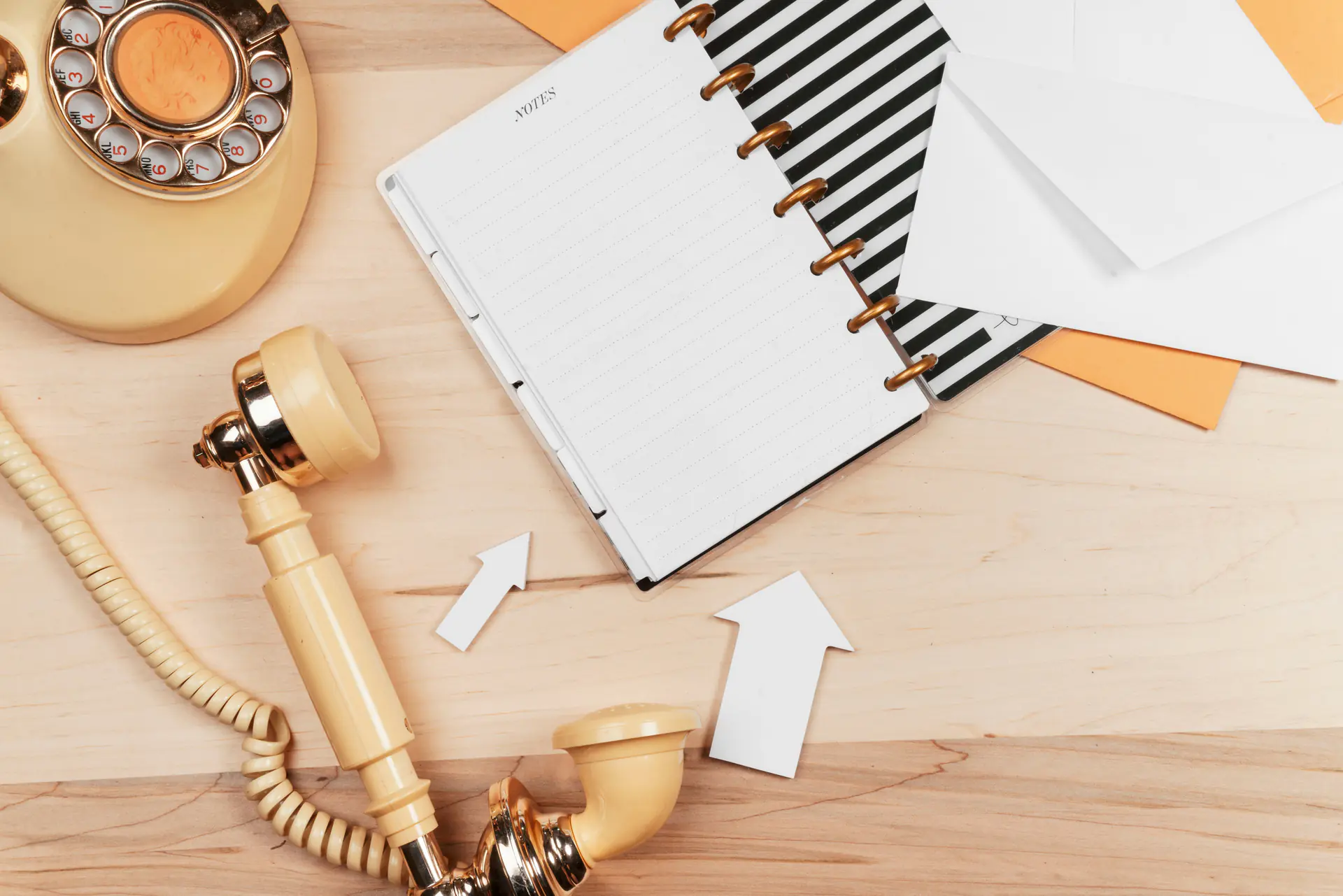 A rotary phone with an open notebook and envelopes on a wooden desk